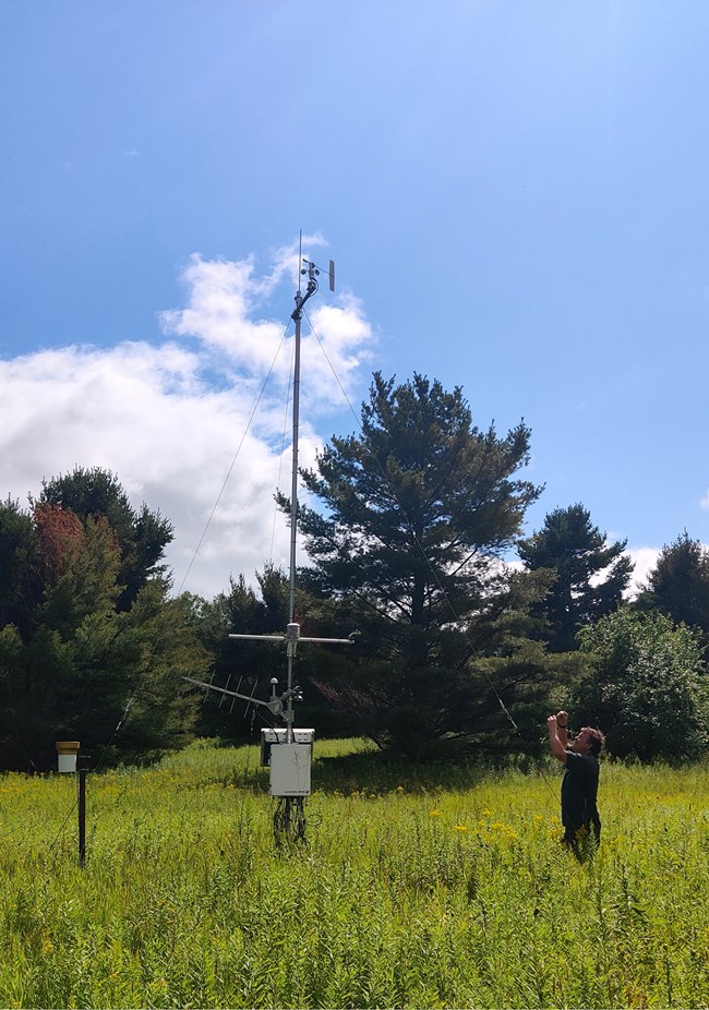 PIRO Weather Station A man is looking up toward the top of a weather station in the middle of a open field.
