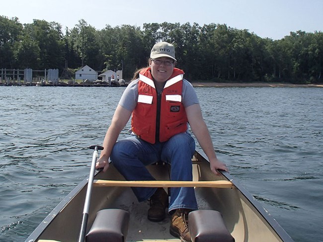 RebeccaKey a woman sits in a canoe on a lake with a dock behind her