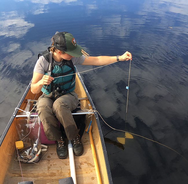 Measuring Secchi depth A woman lowers a disk into a lake while sitting in a canoe