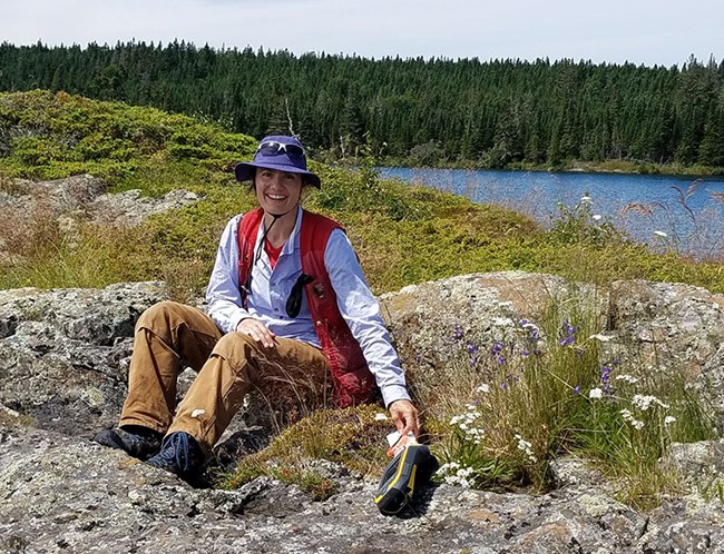 a woman sits among exposed bedrock and low plants