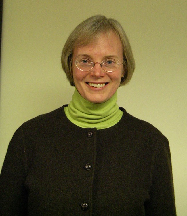a smiling woman stands against a blank wall