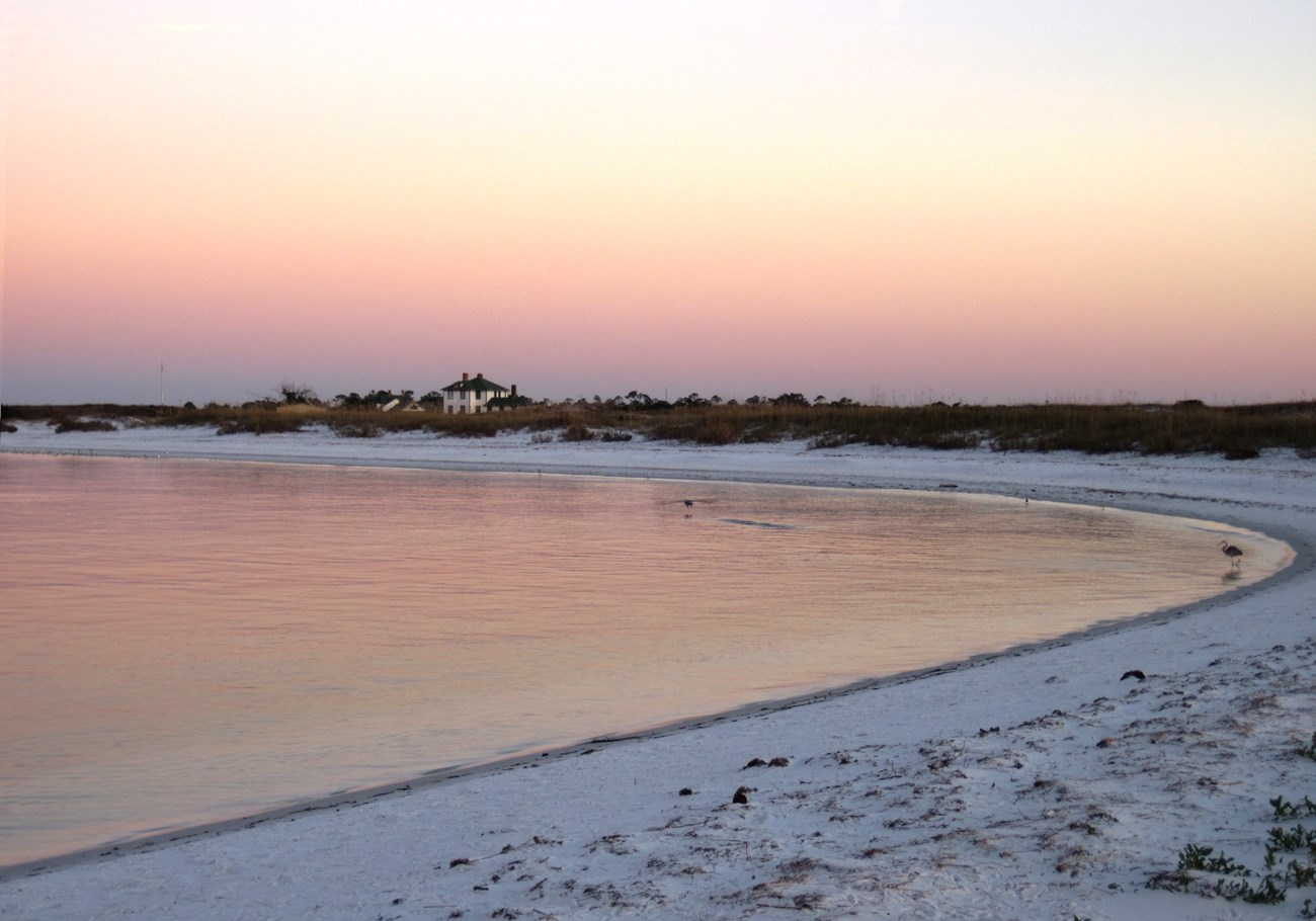 a curving shoreline on a calm, sandy beach at sunset