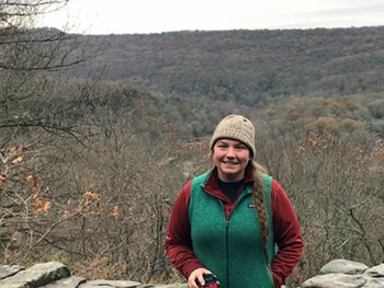 Mary Short A woman standing in front of a landscape of trees across the mountains and valley.