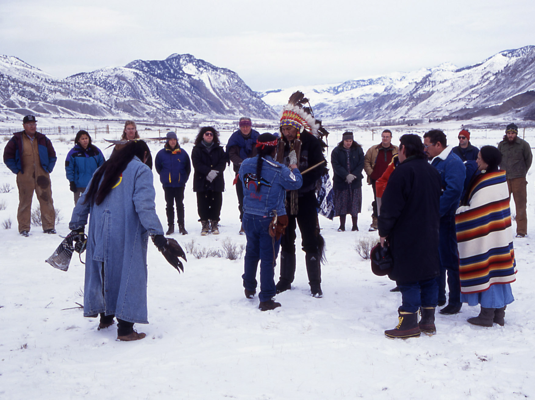 Native American people, some in traditional dress, gather with White people in a snowy mountain landscape. Native American people, some in traditional dress, gather with White people in a snowy mountain landscape.