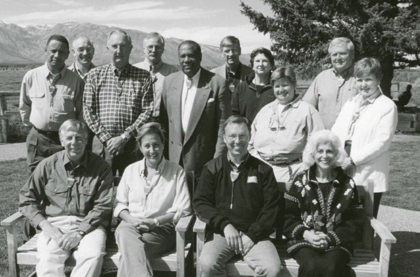 Fourteen smiling men and women pose for a portrait, mountains in background. Fourteen smiling men and women pose for a portrait, mountains in background.