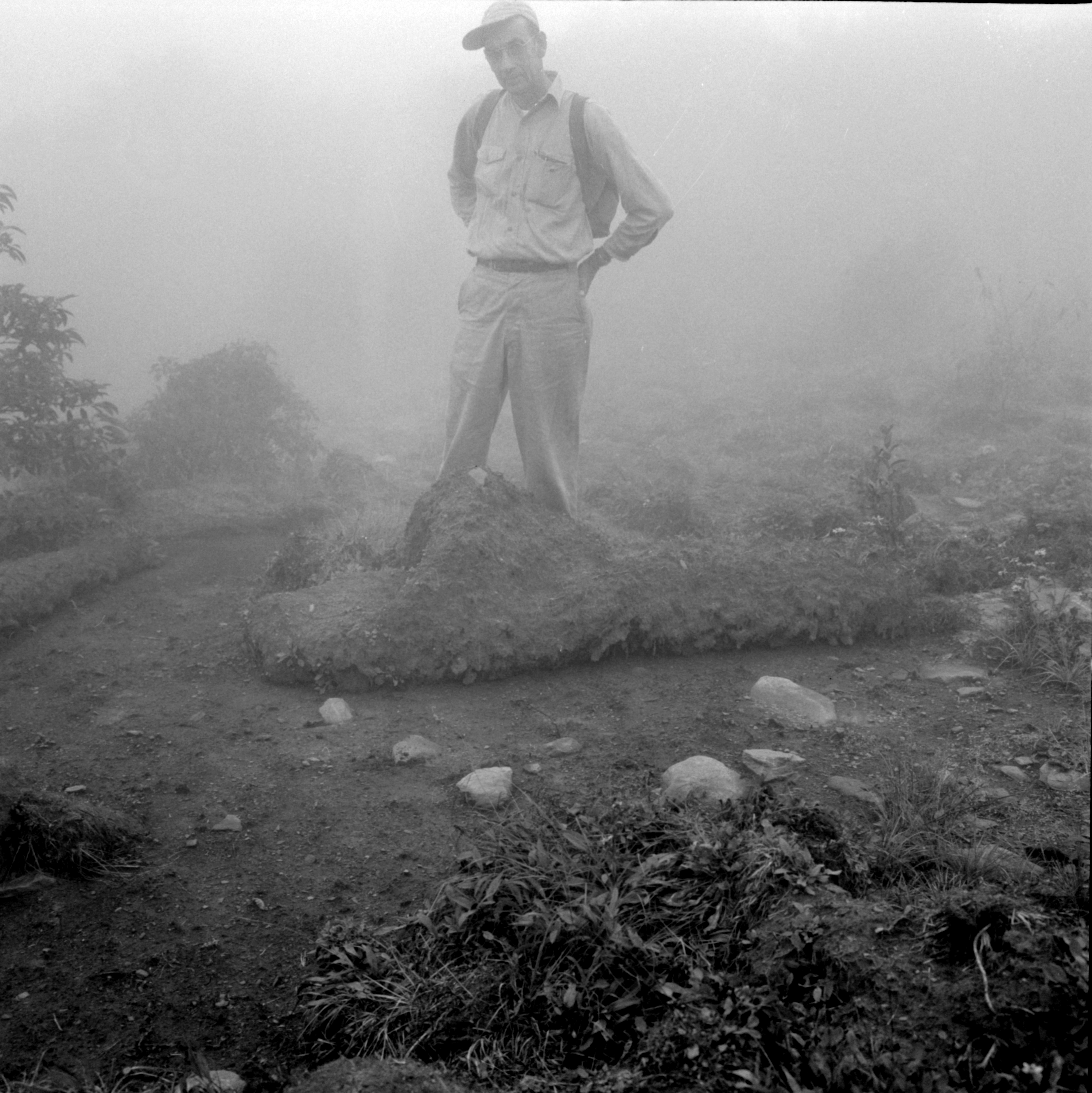 Man in ballcap and backpack stands with his feet obscured by a layer of soil that’s been peeled back from the earth by wild boars.