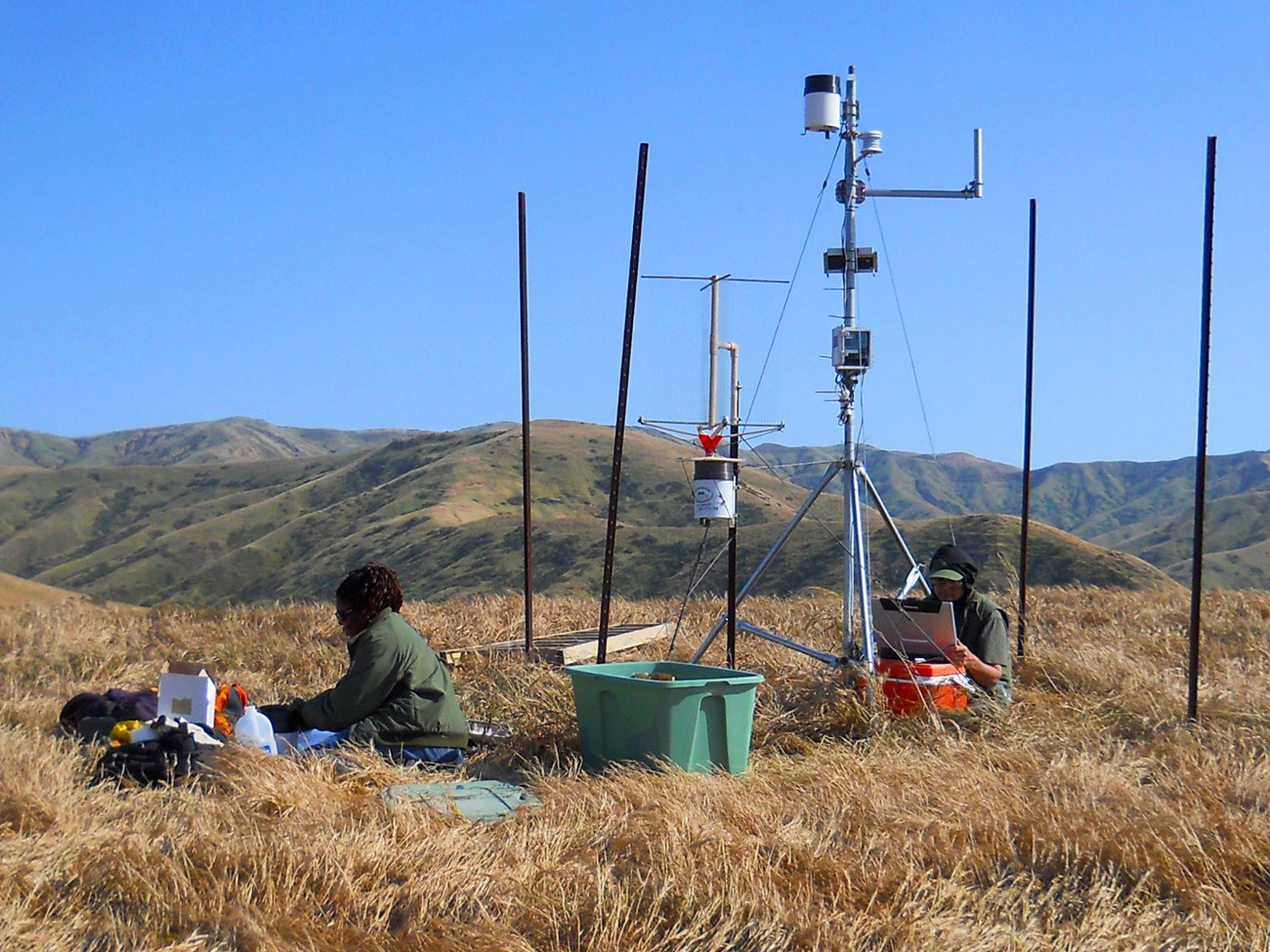 Scientists working on a weather station on a grassy hilltop