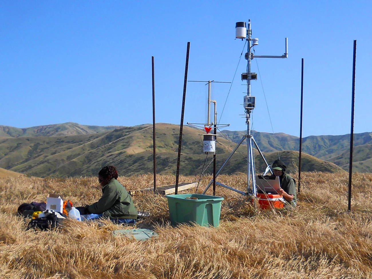 Working on a weather station Scientists working on a weather station on a grassy hilltop