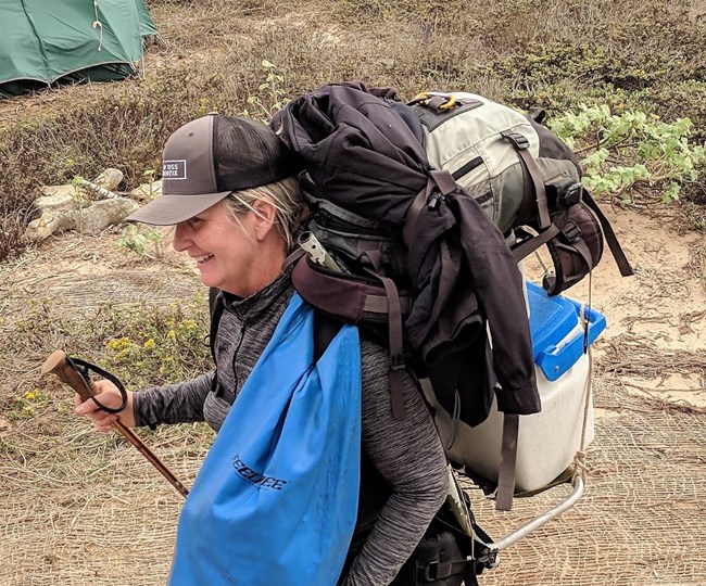 Stacey carrying a ton of gear including a huge pack, a cooler, and a drybag.
