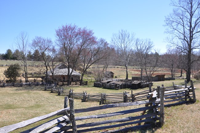 Farm fields dotted with trees and surrounded by stacked wood fences, and a number of small out-buildings, on a clear day