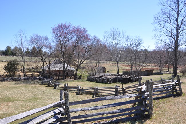 Booker T. Washington National Monument Farm fields dotted with trees and surrounded by stacked wood fences, and a number of small out-buildings, on a clear day