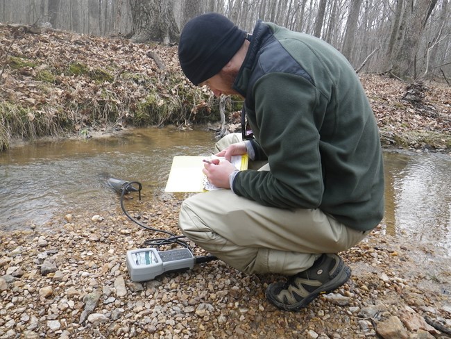 Person with water quality equipment kneeling next to stream