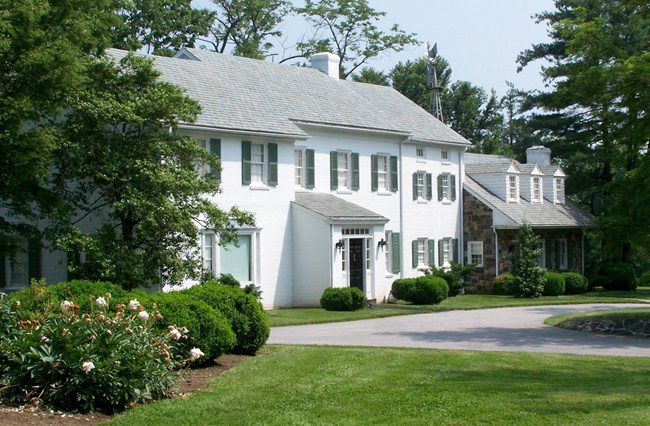 White two-story home surrounded by gardens, yards, and trees