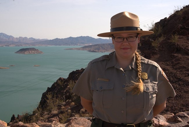 Jennifer Bailard, Physical Scientist, in National Park Service uniform and with large lake in the background.