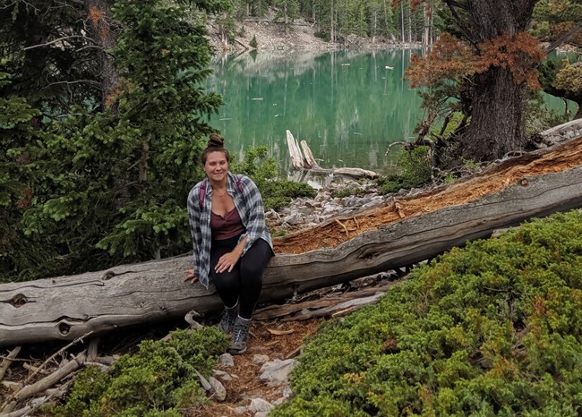Clarice Wheeler, Physical Science Technician Woman with daypack sitting on log in front of small mountain lake