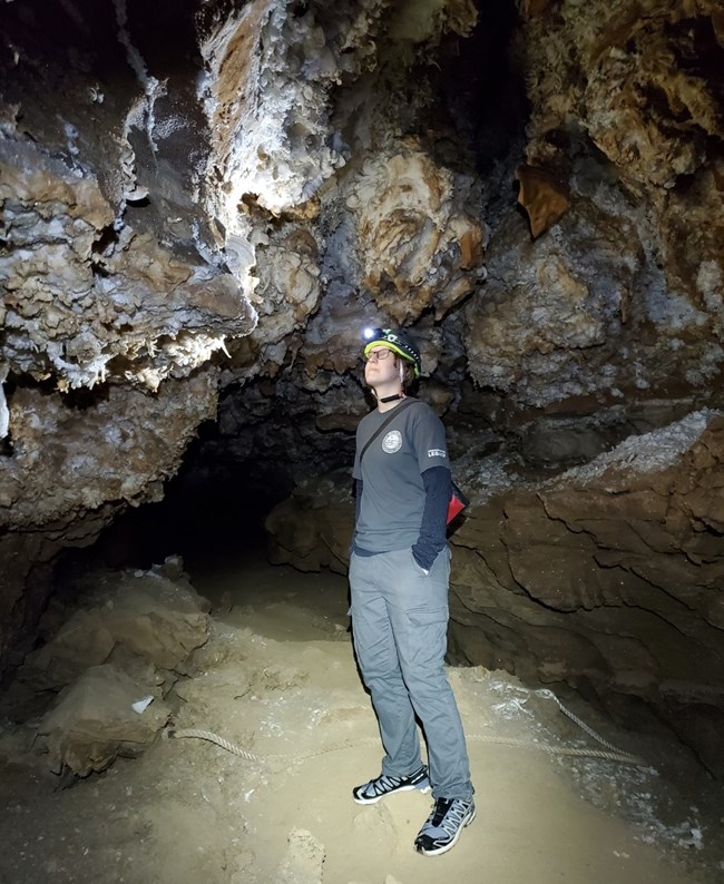 Person in helmet with headlamp standing in a cave and admiring the formations on the cave ceiling.