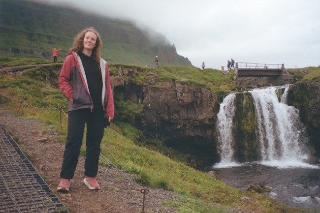 Woman with red raincoat standing in mist next to a waterfall