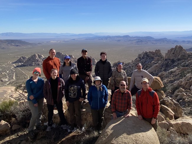 Twelve people standing among boulders on hillside overlooking desert landscape