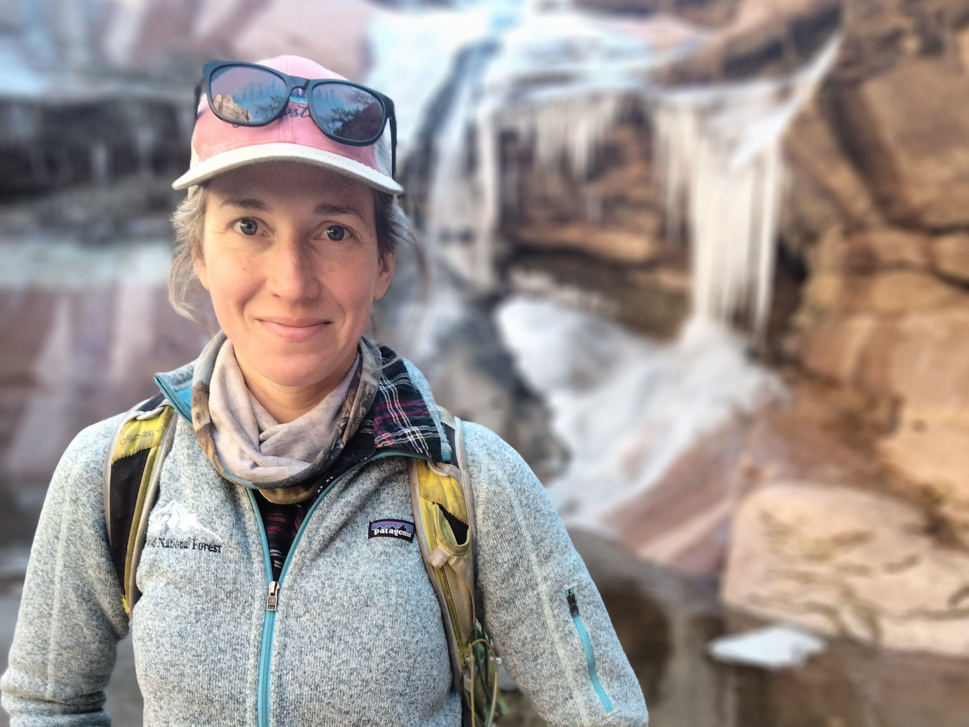 Marisa Monroe, MOJN Physical Science Technician Smiling woman in a baseball cap wearing a backpack and standing in front of a rocky waterfall