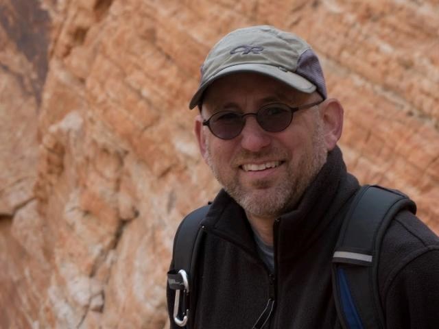 Mark Lehman, Data Manager, wearing a baseball hat and sunglasses with red sandstone formation behind him