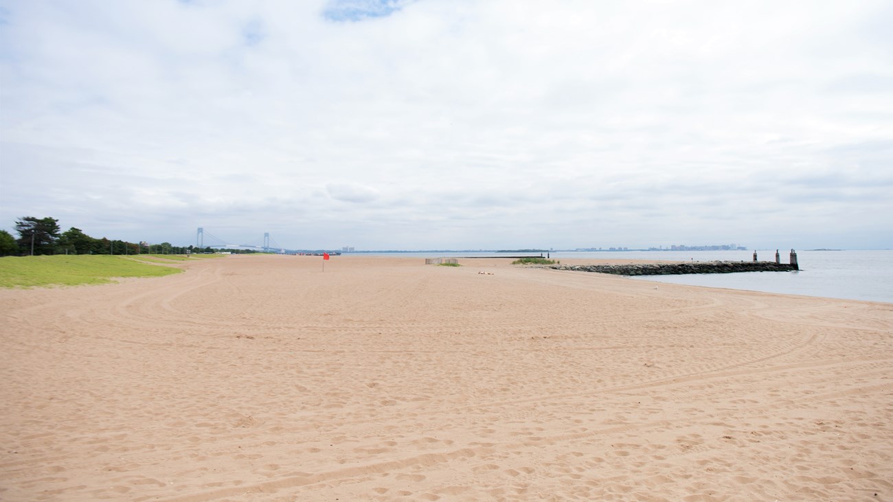 Looking across a beach, with water on the right and a distant bridge behind trees to the left