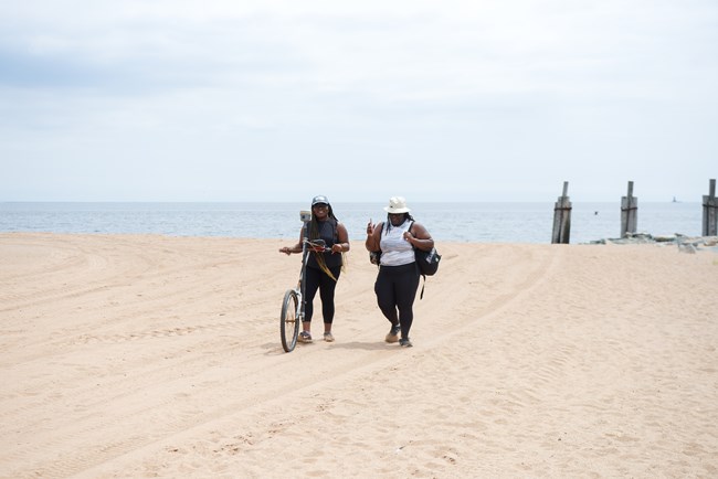 Two interns push a one-wheeled contraption up a beach