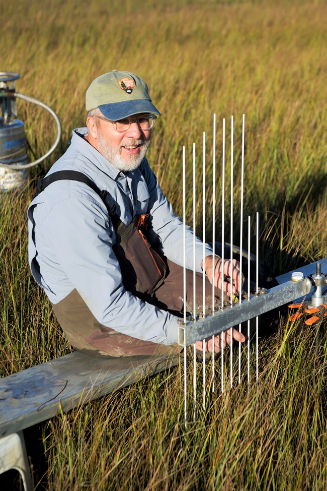 Portrait of field crew member taking measurements with equipment in a salt marsh at sunset