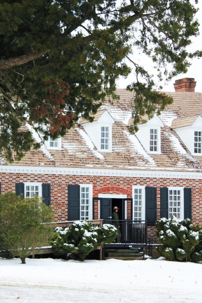 Red brick two-storied house in the snow with a tall tree on the left