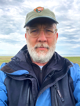 Jim Lynch, NCBN Biologist and Project Lead Jim wearing a blue waterproof jacket and light green NPS cap