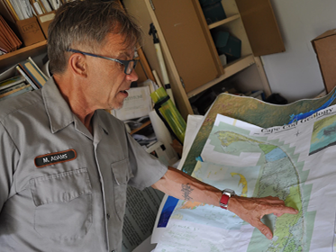 Mark Adams Scientist points to Cape Cod on a map in an office.
