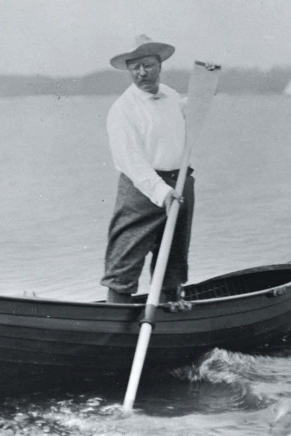Black and white photograph of Theodore Roosevelt holding an oar, standing on a rowboat
