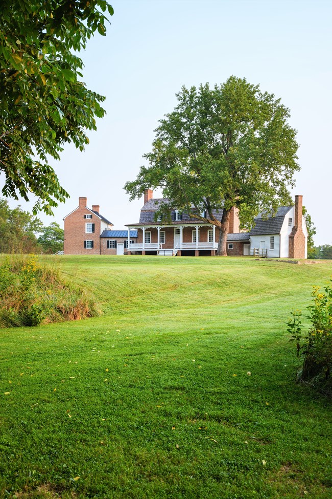 A red bricked house sits at the top of a green hill, with trees on either side