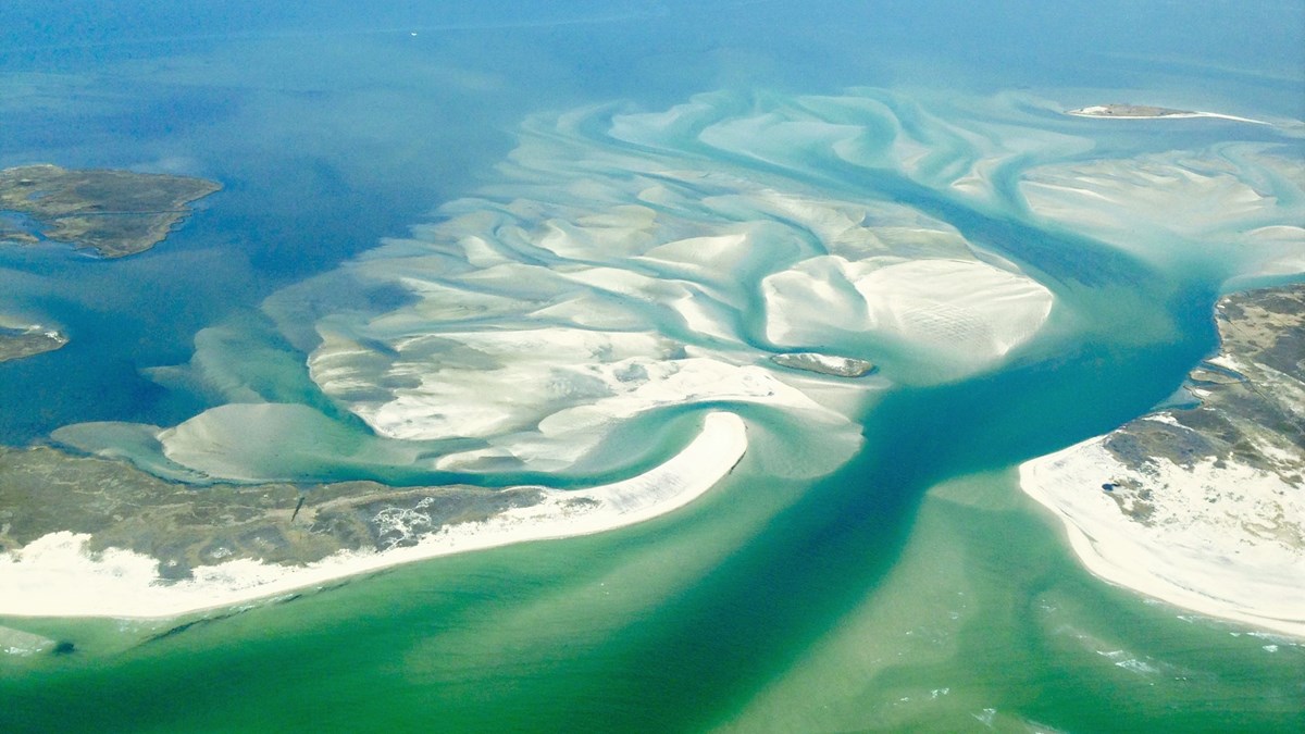Aerial view of sand from portion of a barrier island, swept into a blooming fan shape underwater
