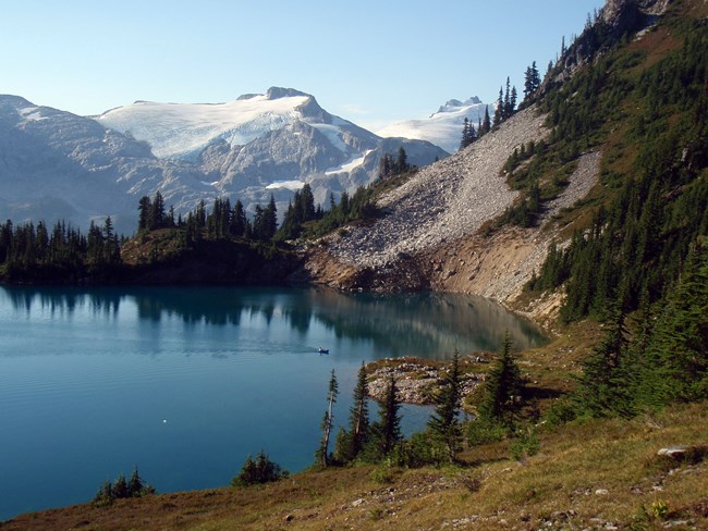 Landscape view of mountain lake with person in inflatable raft and glaciated peak in distance