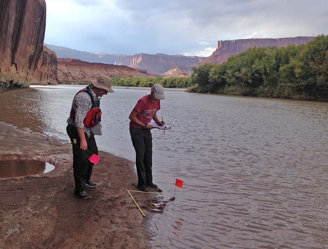 Two people plant pinflags at river's edge