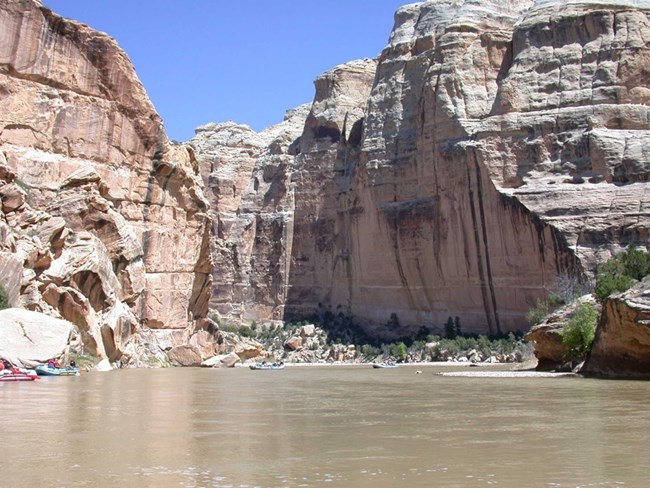 Rafting the Yampa River below Castle Park reveals towering walls carved through layers of deep time. Rafts float on the Yampa River beneath towering canyon walls.