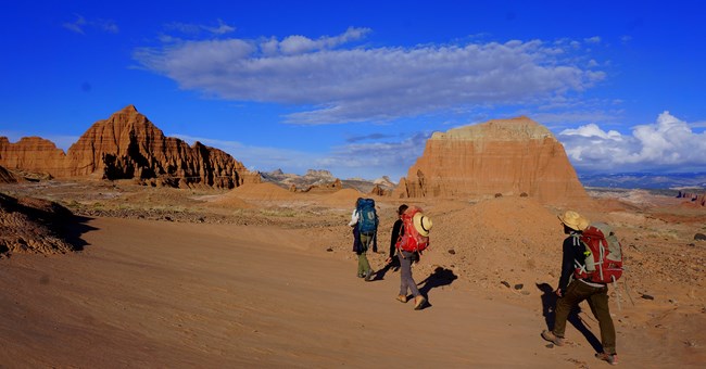People hike through open red rock landscape with brilliant blue sky People hike through open red rock landscape with brilliant blue sky