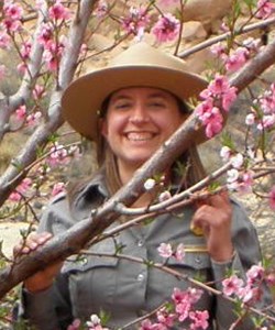 Woman in NPS uniform stands among pink-flowering fruit trees.