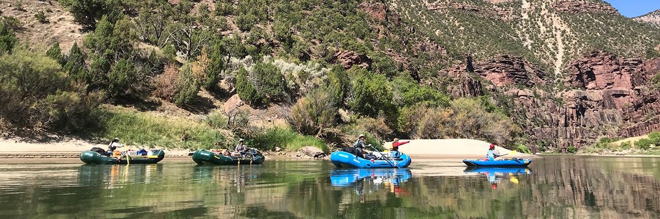 Green River Rafts float down a river with vegetated rock walls and browning tamarisk on the banks
