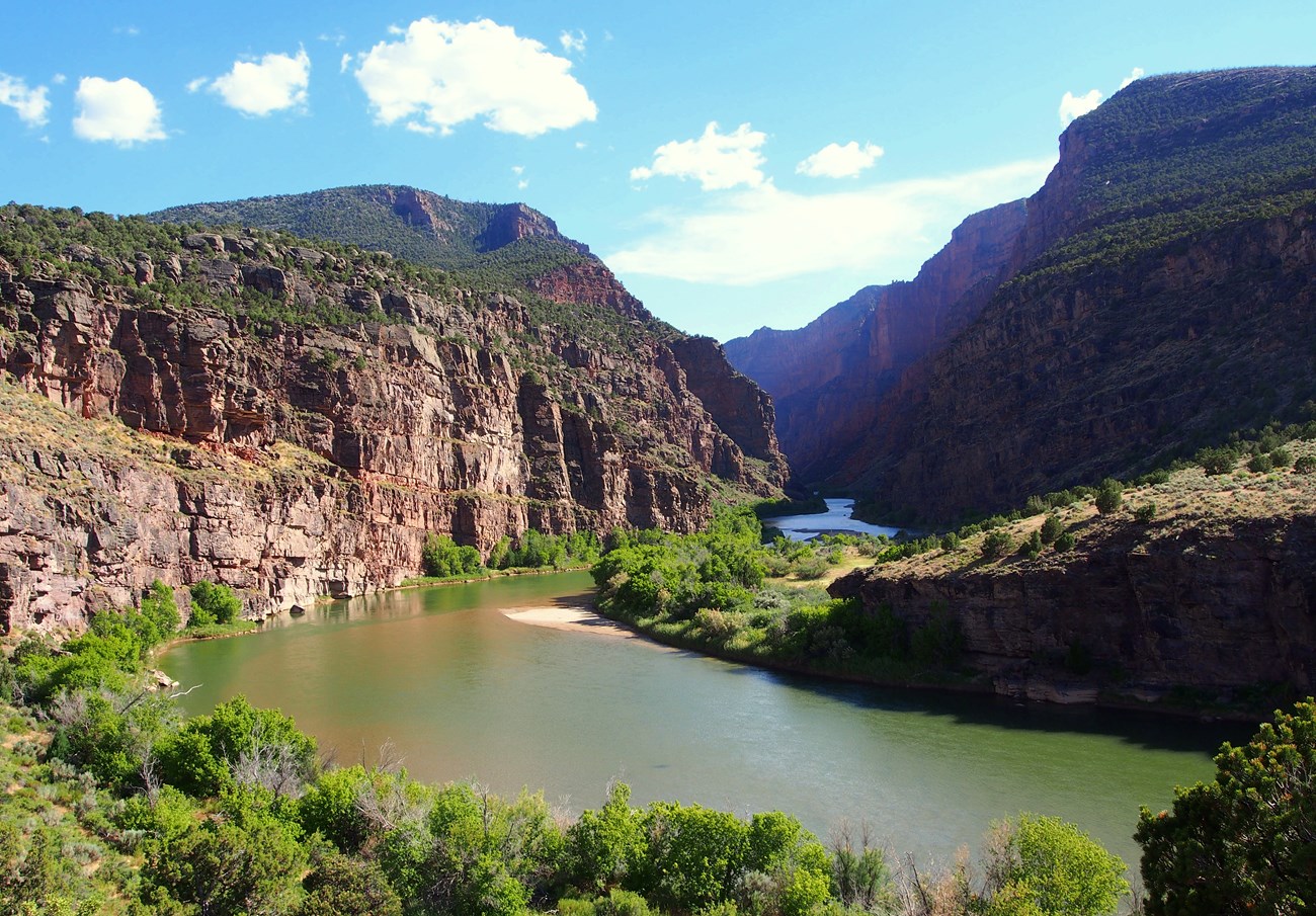 A peaceful river with lush, green vegetation lining its shores meanders through red rock canyon walls. A peaceful river with lush, green vegetation lining its shores meanders through red rock canyon walls.