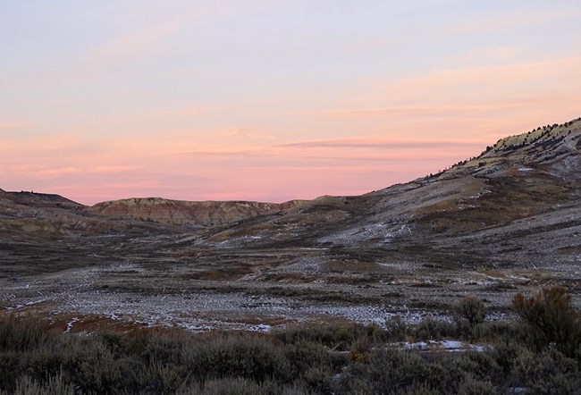 Pink sky over eroded landscape dusted with snow