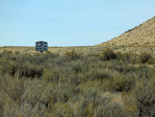 Sagebrush landscape with sign saying "Ten miles of track laid in one day, April 28, 1869." Sagebrush landscape with sign saying "Ten miles of track laid in one day, April 28, 1869."
