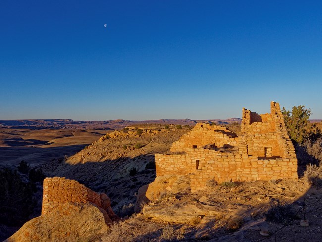 Shelves at Hovenweep NM, Photo: Stephen Bridgehouse Crescent moon at sunset in a deep blue sky above a high desert landscape, with ancestral Puebloan sandstone structures in the foreground on the south end of Cajon Mesa.