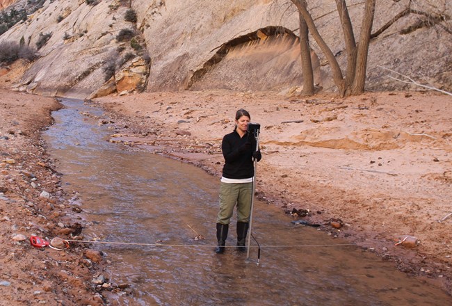 Woman stands in water, taking  measurements at river transect