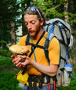 Brandon Gottung Man wearing backpack looking at large mushroom