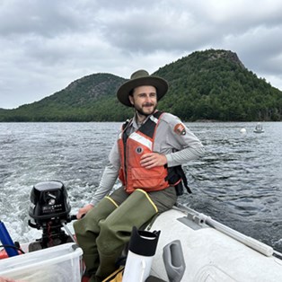Jake_VanGorder pilots a boat on a pristine lake with a mountain in the background.