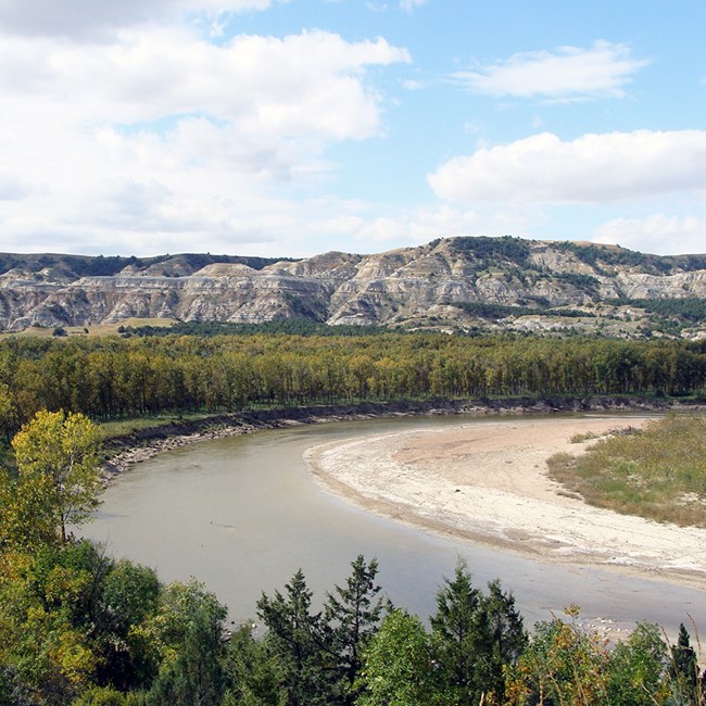 A river bend through forest and badlands topography in the distance