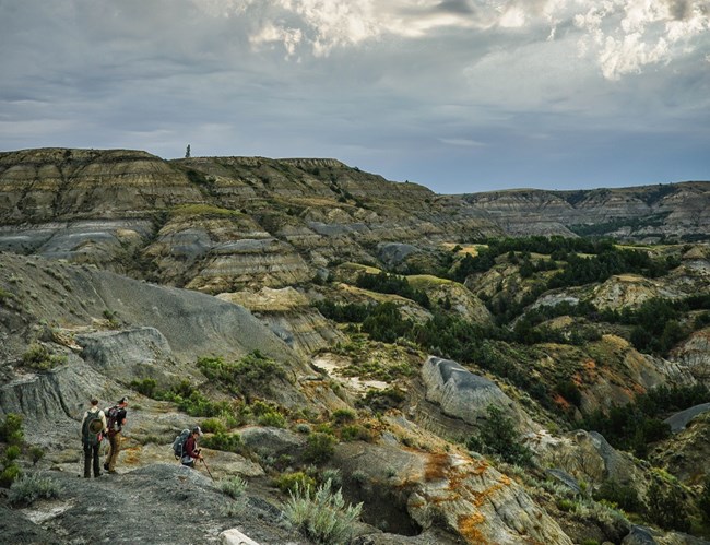 three people hiking in a landscape of eroded bluffs and valleys