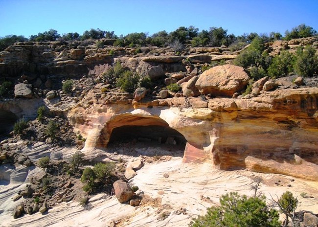View of cliffs with boulder-strewn ledges and a large cave in the lower portion