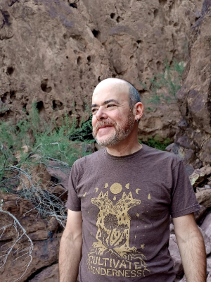 Man in brown shirt standing in front of canyon wall.